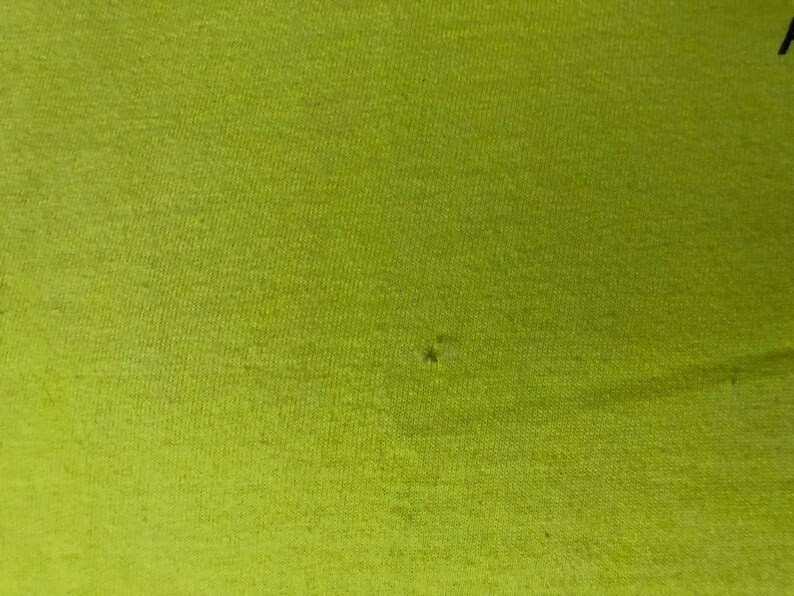May include: A close-up of a bright green fabric with a subtle texture. The fabric has a small hole in the center.