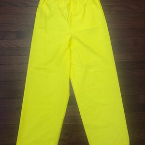 May include: A pair of bright yellow waterproof pants. The pants have an elastic waistband and a relaxed fit.