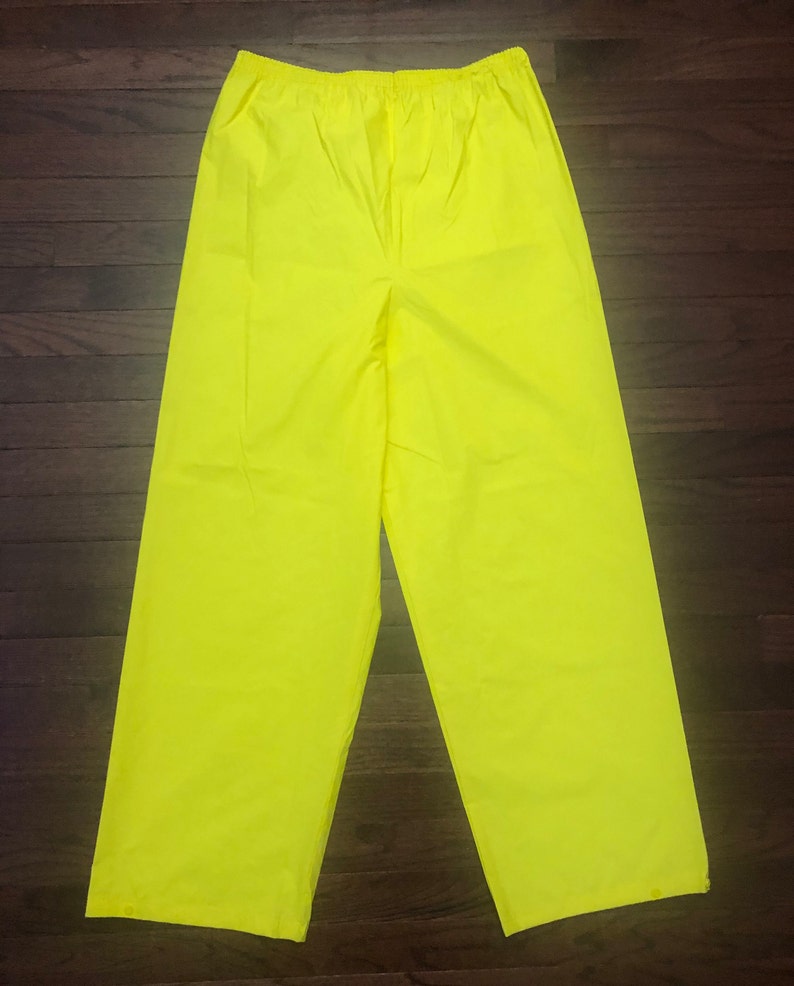 May include: A pair of bright yellow waterproof pants. The pants have an elastic waistband and a relaxed fit.