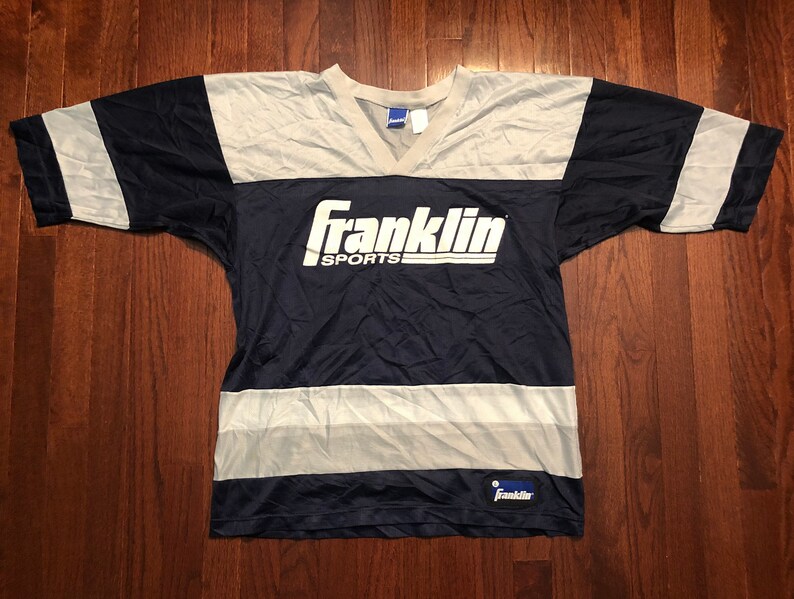 May include: A navy blue and white striped jersey with the text "Franklin Sports" in white on the front. The jersey has a V-neck and short sleeves.