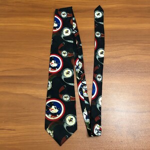 May include: A black silk tie with a repeating pattern of cartoon mice and watches. The mice are wearing red, white, and blue hats and are holding watches. The watches are gold and have Roman numerals.