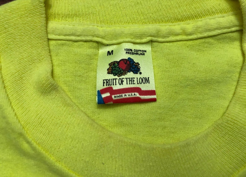 May include: A yellow Fruit of the Loom t-shirt with a tag that says "100% Cotton Preshrunk" and "Fruit of the Loom" with a logo of a bunch of fruit. The tag also says "Made in U.S.A." and "M" for size.