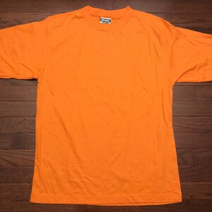 May include: A bright orange short-sleeved t-shirt with a Simply Style tag on the front.