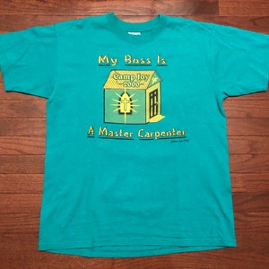 May include: A teal blue t-shirt with a yellow and green graphic of a house with the text "My Boss Is Camp Joy 2000 A Master Carpenter".