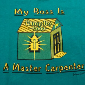May include: Teal blue t-shirt with a yellow and green illustration of a church with the text "Camp Joy - 2000" on the roof. The text "My Boss Is A Master Carpenter" is printed below the illustration. The text "Catherine Jane O'Neil" is printed in smaller font below the main text.