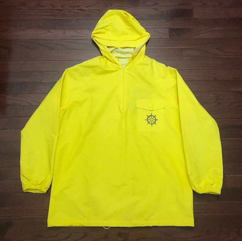 May include: A bright yellow hooded jacket with a black compass design on the front pocket. The jacket has a half zipper and elastic cuffs.