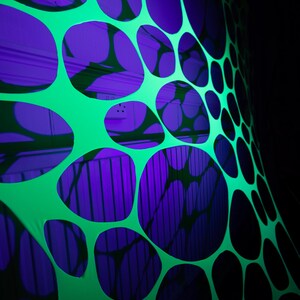 May include: A vibrant, abstract design featuring a neon green fabric with large, irregular, oval-shaped cutouts. The cutouts reveal a deep purple background, creating a striking contrast. The overall effect is a modern, eye-catching pattern.