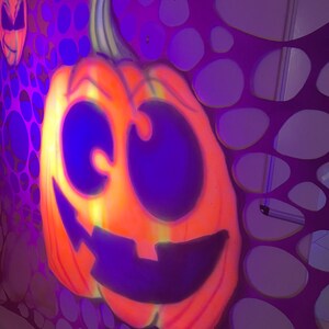 Pu&ograve; includere: Una grande zucca arancione con un ghigno intagliato a denti e occhi grandi &egrave; dipinta su uno sfondo viola con un motivo di cerchi sovrapposti.