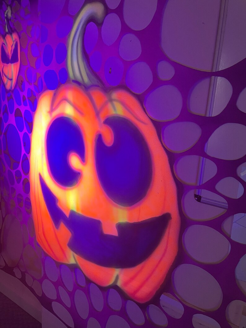 Pu&ograve; includere: Una grande zucca arancione con un ghigno intagliato a denti e occhi grandi &egrave; dipinta su uno sfondo viola con un motivo di cerchi sovrapposti.