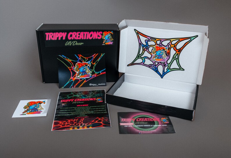 Pu&ograve; includere: Una scatola nera con la scritta "Trippy Creations UV Decor" sul davanti. La scatola &egrave; aperta e contiene un adesivo colorato con un personaggio dei cartoni animati. L'adesivo &egrave; su uno sfondo bianco. Ci sono anche altri due adesivi con lo stesso personaggio.