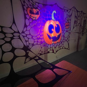 Pu&ograve; includere: Una decorazione a ragnatela nera con una zucca arancione incandescente con un viso di zucca intagliata. La zucca &egrave; illuminata da una luce viola.