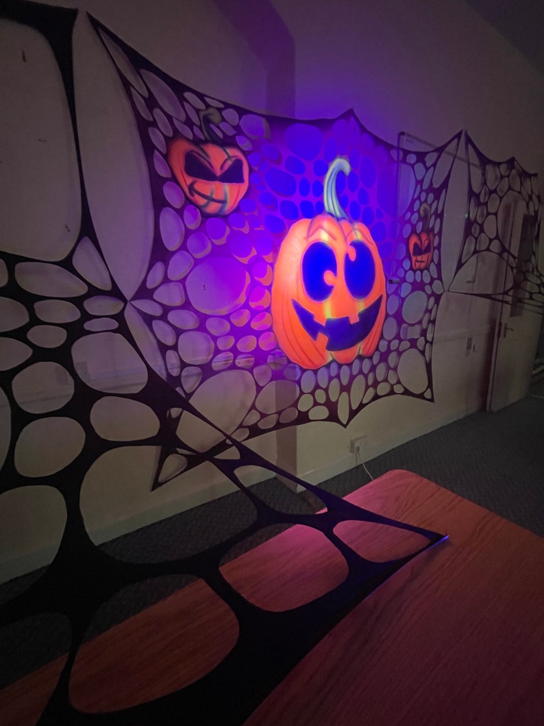 Pu&ograve; includere: Una decorazione a ragnatela nera con una zucca arancione incandescente con un viso di zucca intagliata. La zucca &egrave; illuminata da una luce viola.