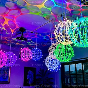 Op de afbeelding: Een verzameling bolvormige, verlichte decoratieve lichten in verschillende kleuren, waaronder roze, blauw, groen en wit. De lichten hangen aan het plafond en creëren een levendige en kleurrijke weergave. Het plafond is versierd met een kleurrijk, abstract patroon.