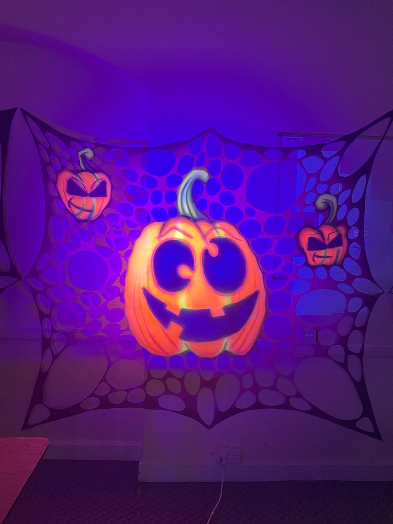 Pu&ograve; includere: Tre zucche arancioni a forma di jack-o'-lantern con occhi e bocche nere sono appese a una ragnatela nera su uno sfondo viola.