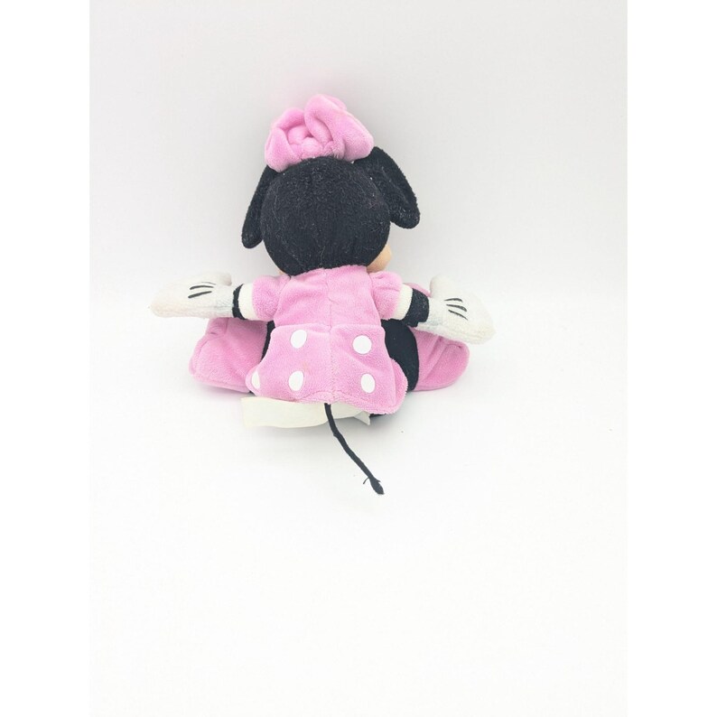 Puede incluir: Juguete de peluche Minnie Mouse rosa con lunares blancos, orejas negras y un lazo rosa.