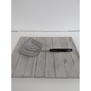 May include: A stainless steel spatula with a black handle. The spatula has a wide, slotted head with several small holes. The handle is curved and has a hole at the end for hanging. The spatula is designed for cooking.