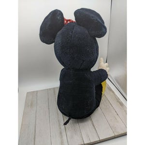 May include: A black plush Mickey Mouse toy with red polka dot bow sitting on a wooden surface.