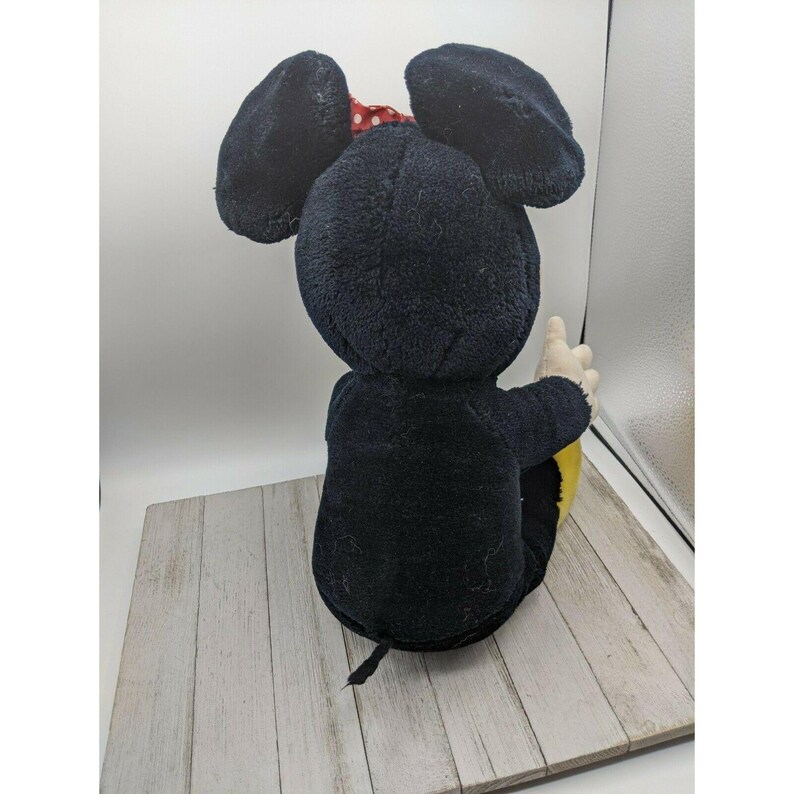 May include: A black plush Mickey Mouse toy with red polka dot bow sitting on a wooden surface.