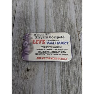May include: A white rectangular sign with blue and red text that reads "Watch NFL Players Compete Exclusively At LIVE WALMART. The Fifth Annual "Game Before The Game" Thursday, January 27th Home Entertainment Dept. Ask Me For More Details."