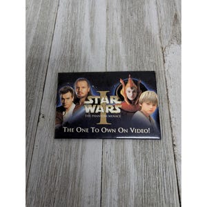 May include: A black and gold Star Wars Episode I: The Phantom Menace VHS tape. The image features characters from the film, including Qui-Gon Jinn, Obi-Wan Kenobi, Padmé Amidala, and Anakin Skywalker. The text on the tape reads "The One To Own On Video!"