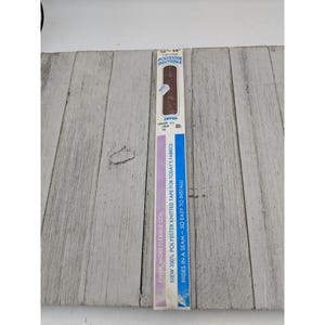 May include: A package of brown polyester invisible zipper tape, with text that reads "FINER, MORE FLEXIBLE COIL" and "NEW 100% POLYESTER KNITTED TAPE FOR TODAY'S FABRICS". The package is on a light gray wooden surface.