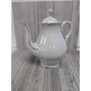 May include: White porcelain teapot with a gold trim and a lid. The teapot has a classic design and is perfect for serving tea.