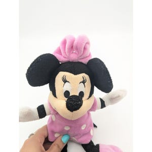 Puede incluir: Juguete de peluche Minnie Mouse rosa y negro con un lazo rosa. Lleva un vestido rosa con lunares blancos.