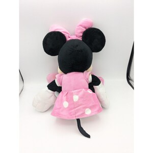 Op de afbeelding: Een roze pluche Minnie Mouse speelgoed met witte stippen op haar jurk en een zwarte strik op haar hoofd.