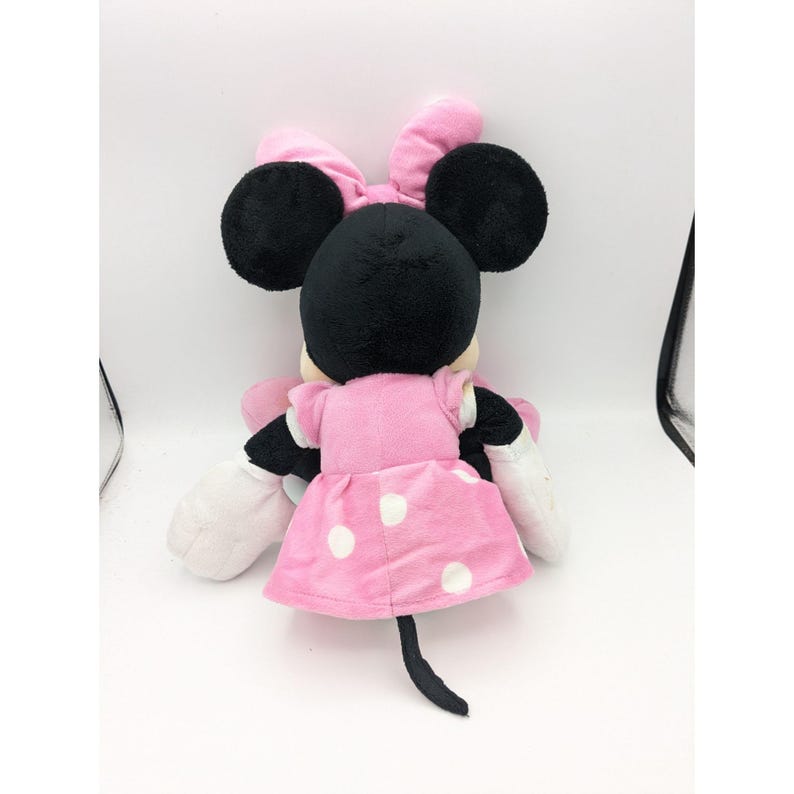 Op de afbeelding: Een roze pluche Minnie Mouse speelgoed met witte stippen op haar jurk en een zwarte strik op haar hoofd.