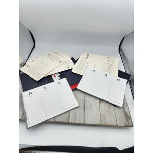 May include: A set of white notepads with black lines and a black and white graphic of a person's face on the cover. The notepads are on a wooden surface.