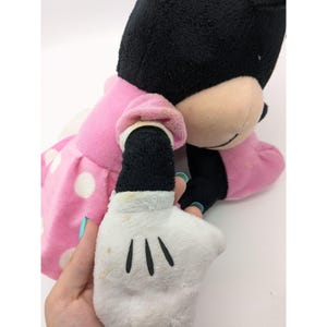 Op de afbeelding: Een roze jurk met witte stippen en zwarte accenten. De jurk wordt gedragen door een pluche Minnie Mouse speelgoed. Het speelgoed heeft zwarte oren, een zwarte neus en witte handschoenen.