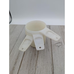 May include: A set of three white plastic measuring cups. The cups are nested together and have a handle on each side.