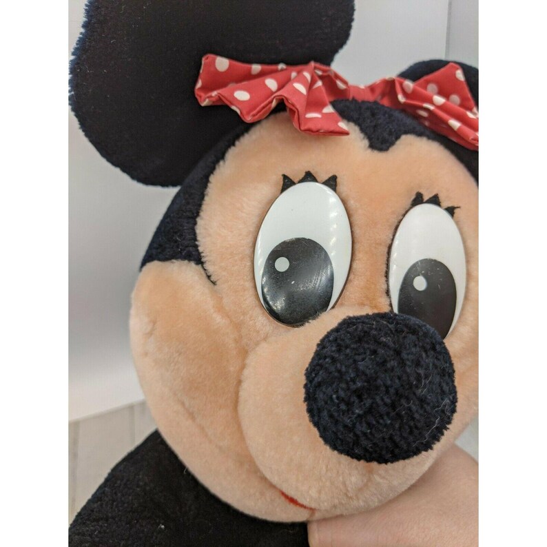 May include: A plush toy of Mickey Mouse's girlfriend Minnie Mouse. She has a black nose, large black eyes, and a red bow with white polka dots.