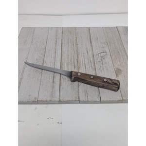 Könnte beinhalten: Ein Ausbeinmesser aus Edelstahl mit Holzgriff. Das Messer hat eine lange, dünne Klinge und einen dunkelbraunen Griff mit zwei Nieten. Das Messer liegt auf einer hellgrauen Holzoberfläche.