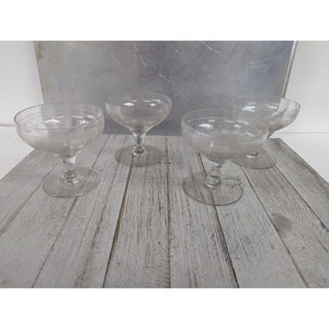 May include: Four clear glass dessert cups with etched designs on a light wood surface.