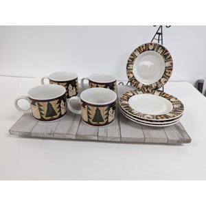 May include: A set of four mugs and four plates with a Christmas theme. The mugs and plates have a brown border with a repeating pattern of Christmas trees and snowmen. The mugs have white interiors and handles.