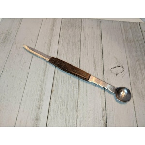May include: A vintage stainless steel melon baller and knife combination tool. The tool has a wooden handle and a serrated knife blade on one end. The other end features a round, concave scoop for balling melons. The tool is designed for preparing fruit.
