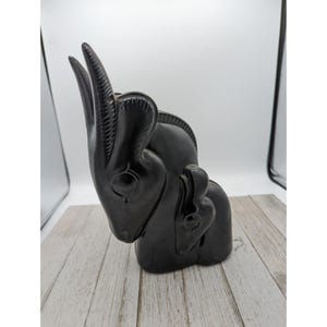 Puede incluir: Escultura de madera tallada en negro de dos animales estilizados, uno más grande que el otro, con un acabado liso y pulido.