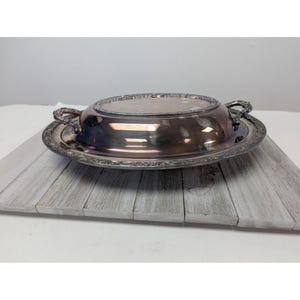May include: Silver oval serving dish with a lid and two handles. The dish has a decorative border.