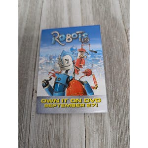 May include: A DVD cover for the animated movie "Robots" featuring two robots, one blue and one red, against a cityscape background. The text "Own it on DVD September 27!" is at the bottom.