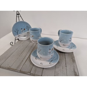 May include: Set of three blue and white ceramic teacups and saucers with a winter scene design. Each cup and saucer features a snowman, trees, and footprints in the snow.
