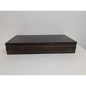 May include: A dark brown wooden box with a hinged lid. The box has a simple design with a smooth surface and a slightly raised edge around the top.