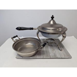 May include: Silver chafing dish with a black handle and a lid. The chafing dish is on a wooden stand with a white wash finish.
