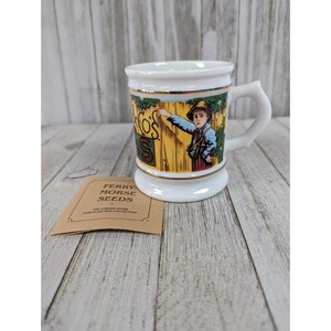 May include: White ceramic mug with a gold rim and a colorful illustration of a boy pointing to a sign that says "Ferry Morse Seeds". The mug is part of a porcelain mini collection from The Corner Store.