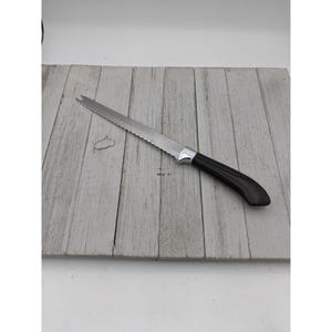 May include: A bread knife with a serrated blade and a black handle. The knife has a silver blade and a curved handle. The knife is designed for slicing bread and other baked goods. The handle is approximately 15 cm long.