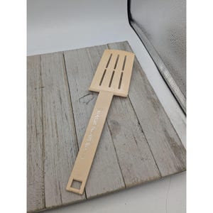 Op de afbeelding: Een beige plastic spatel met een gesleufde kop en een handvat met de tekst "B.B.B. CO. PAT. 4,151,579".