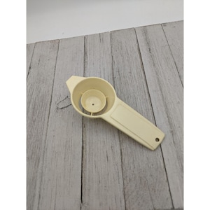 May include: A cream-colored egg separator made of plastic. The separator has a large bowl with a smaller bowl in the center, and a handle with a hole at the end. The kitchen utensil is designed to separate egg whites from yolks.