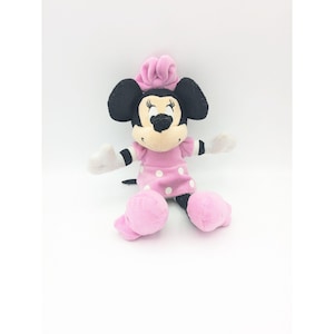 Puede incluir: Un juguete de peluche rosa y negro de Minnie Mouse con un vestido rosa con lunares blancos.