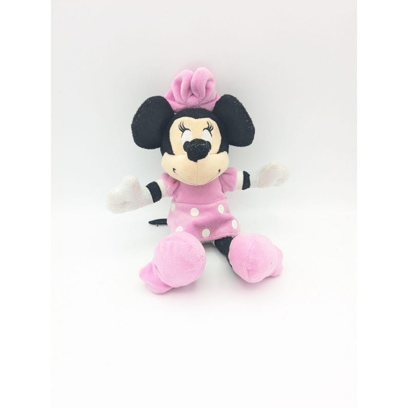 Puede incluir: Un juguete de peluche rosa y negro de Minnie Mouse con un vestido rosa con lunares blancos.