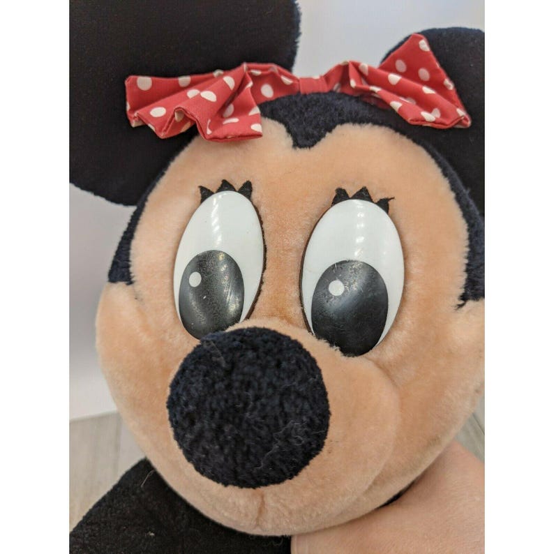 May include: A plush toy of a cartoon mouse with large black eyes, a black nose, and a red bow with white polka dots.